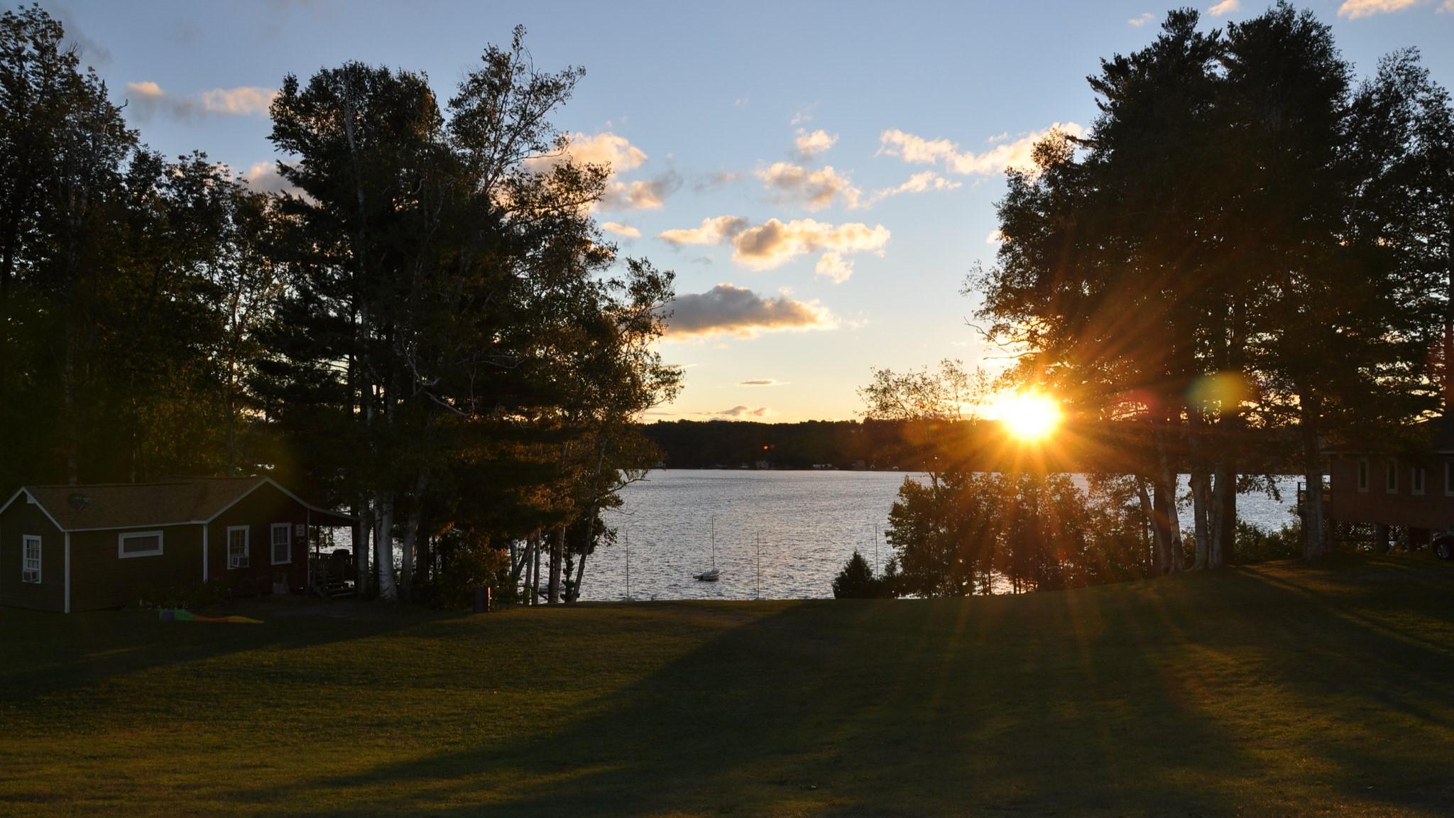 夕阳落在湖滨的景色上, 有一个小木屋, 绿色的草坪, 还有岸边的树木